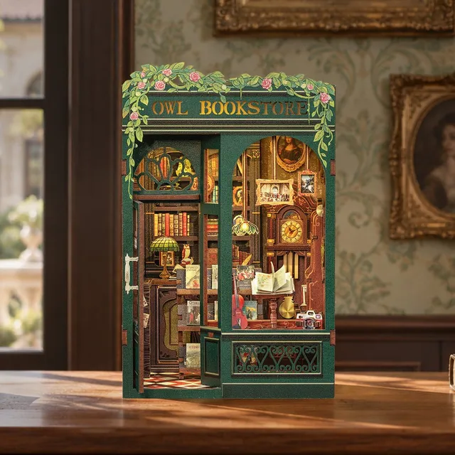 Book nook Owl Bookstore monté, devanture verte fleurie, posé sur un bureau ancien