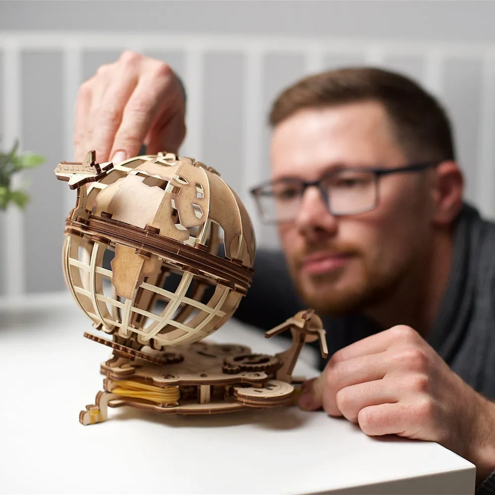 Un homme à lunettes fait tourner le globe en bois posé sur une table blanche