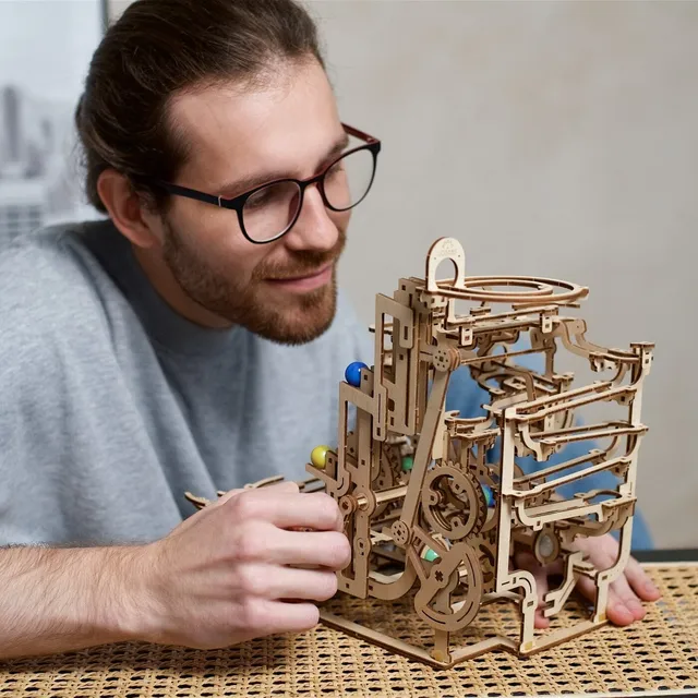Un homme à lunettes termine le circuit à billes en bois posé sur une table