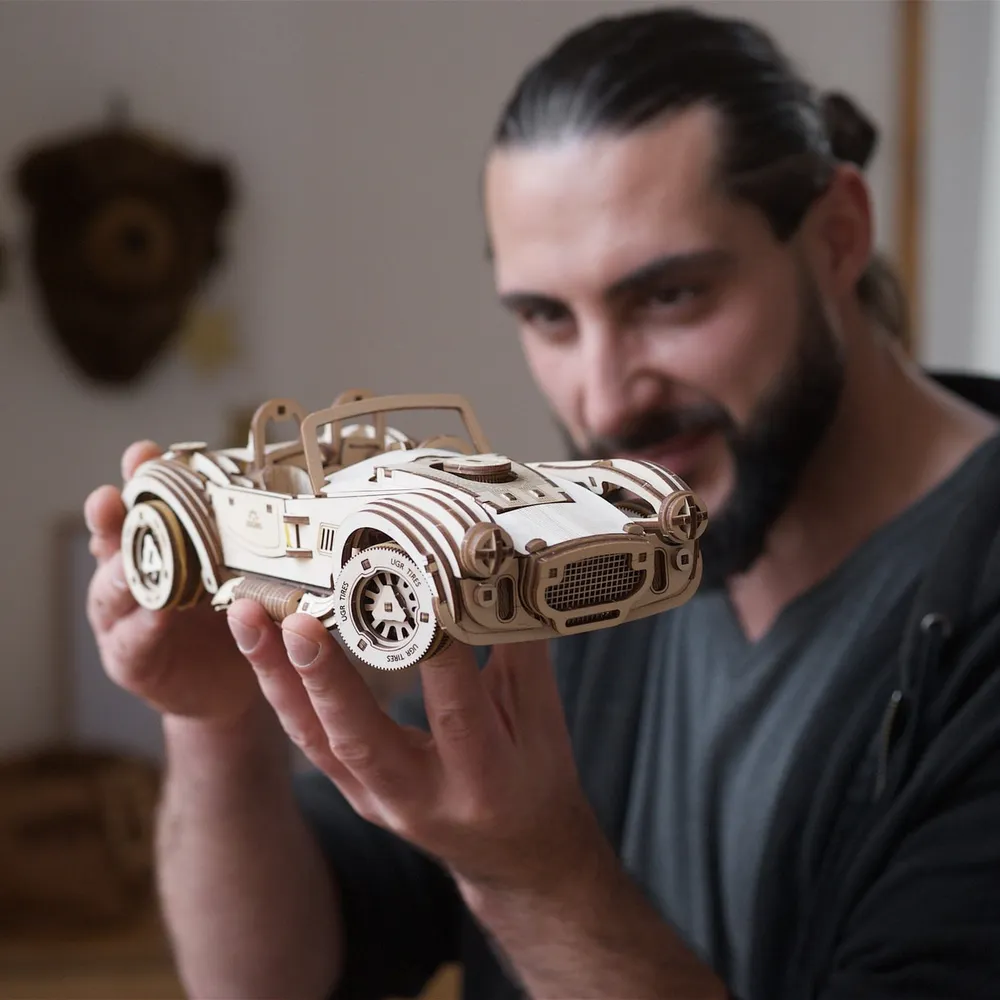 Un homme barbu tient la voiture en bois dans ses mains et la regarde de près