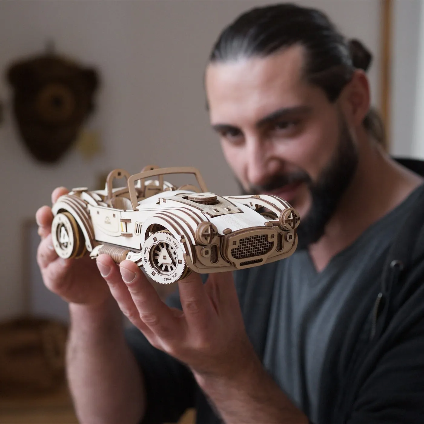 Un homme barbu tient la voiture en bois dans ses mains et la regarde de près