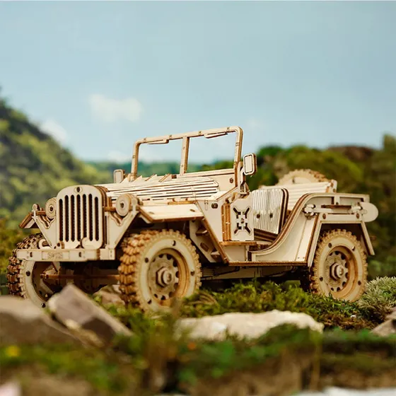La jeep en bois posée parmi les rochers et la végétation, devant un ciel de montagne