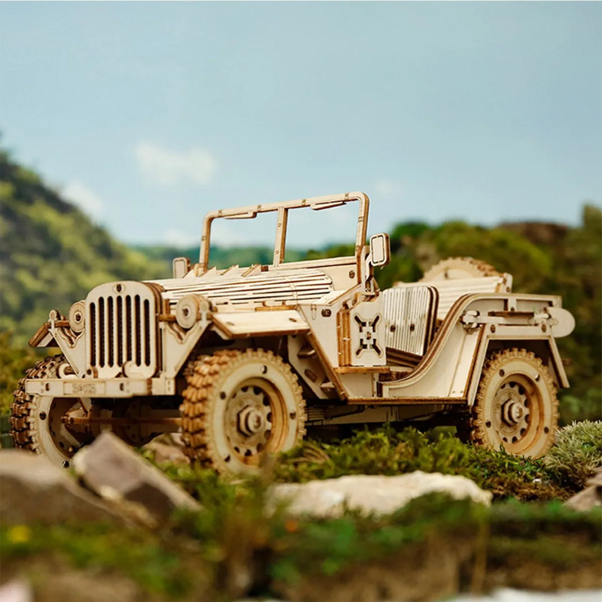 La jeep en bois posée parmi les rochers et la végétation, devant un ciel de montagne
