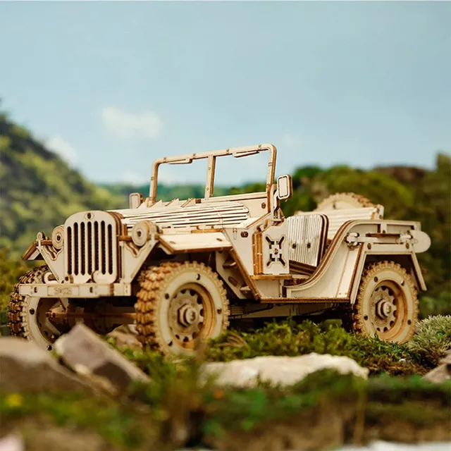 La jeep en bois posée parmi les rochers et la végétation, devant un ciel de montagne