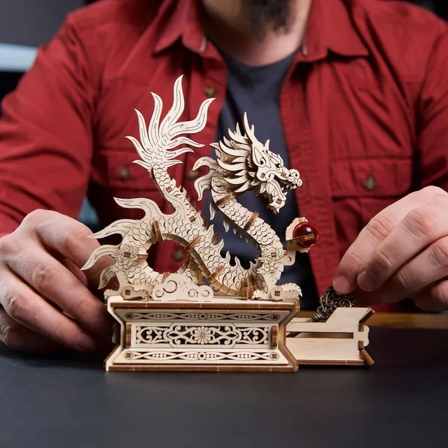 Un homme en chemise rouge ouvre le tiroir secret du socle, le dragon de bois dressé au-dessus