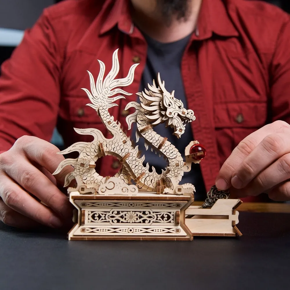 Un homme en chemise rouge ouvre le tiroir secret du socle, le dragon de bois dressé au-dessus