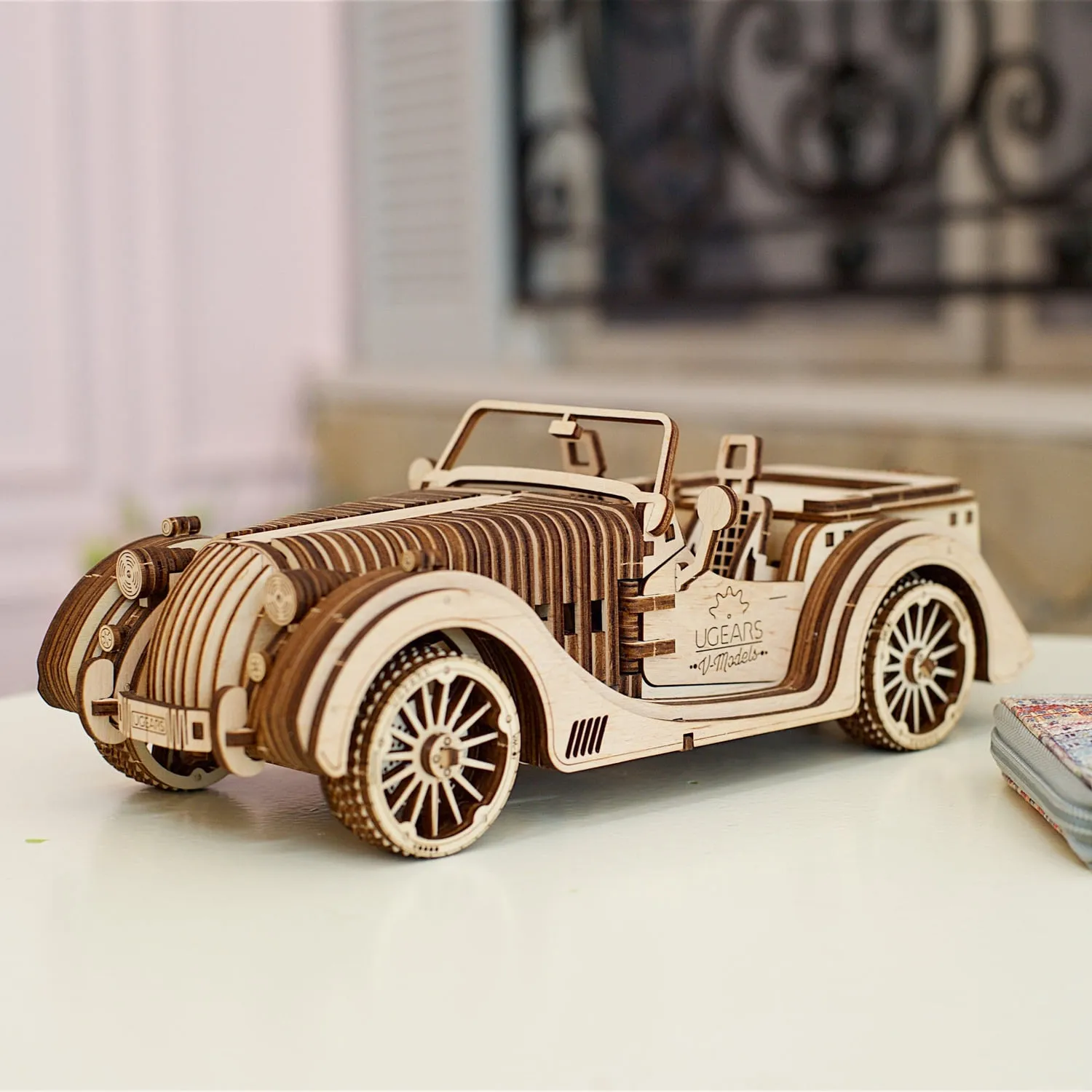 Cabriolet en bois sur une table blanche devant une fenêtre à ferronnerie floutée