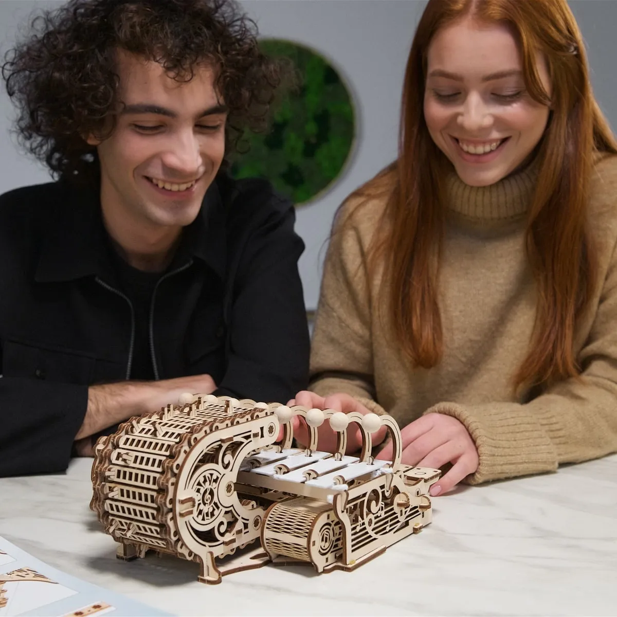 Un jeune homme et une jeune femme souriants jouent sur le clavier du célesta en bois posé sur une table