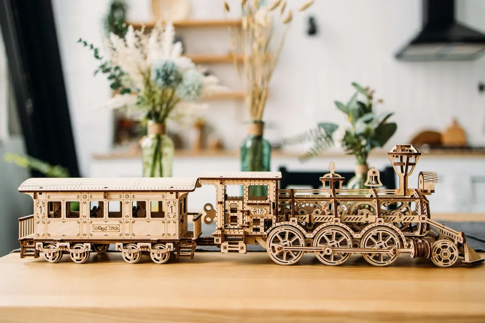 La locomotive et son wagon posés sur une table en bois, devant une cuisine décorée de fleurs séchées