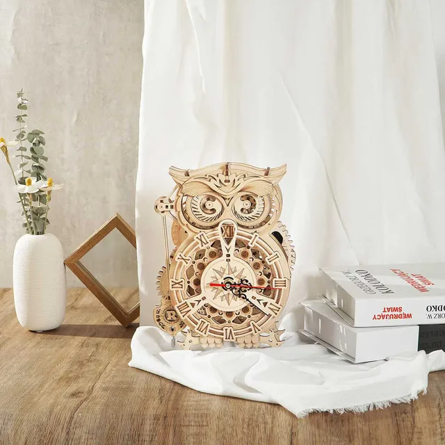Horloge hibou sur une table en bois entre un vase de fleurs séchées, un cadre et des livres