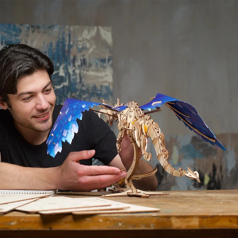 Un homme souriant ajuste les ailes du dragon en bois posé sur son établi