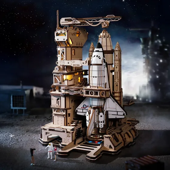 La base de lancement éclairée de nuit, navette à la verticale, petits personnages au pied de la tour