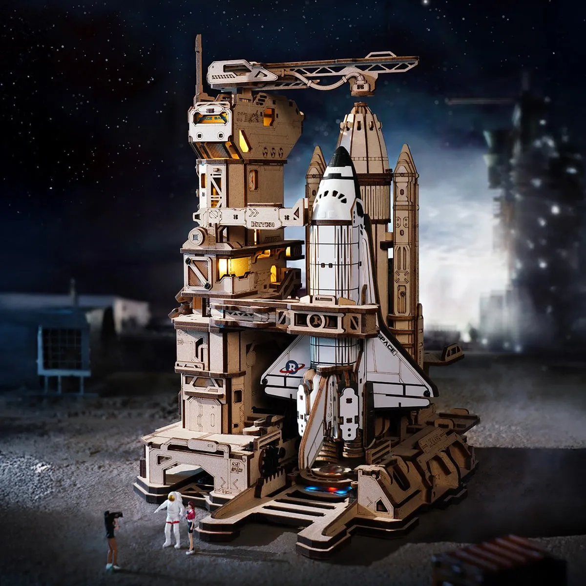 La base de lancement éclairée de nuit, navette à la verticale, petits personnages au pied de la tour