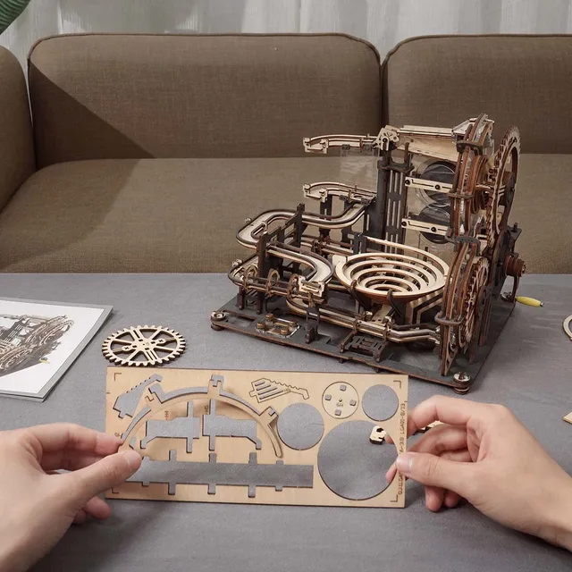 Le circuit terminé sur une table de salon, deux mains détachent des pièces de bois