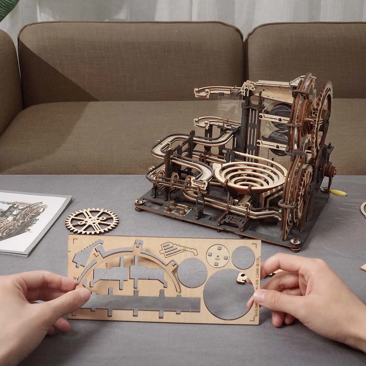 Le circuit terminé sur une table de salon, deux mains détachent des pièces de bois