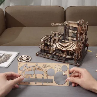 Le circuit terminé sur une table de salon, deux mains détachent des pièces de bois