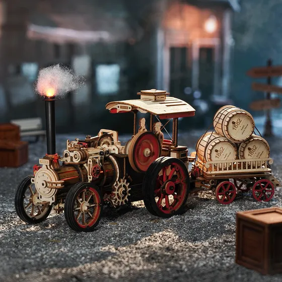 La locomobile et sa remorque sur un sol de gravier devant des maisons de village, fumée à la cheminée