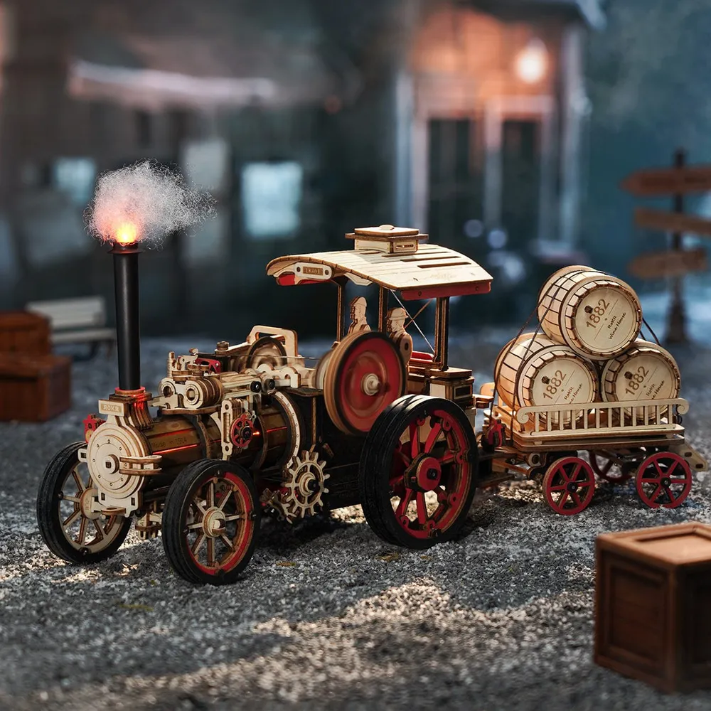 La locomobile et sa remorque sur un sol de gravier devant des maisons de village, fumée à la cheminée