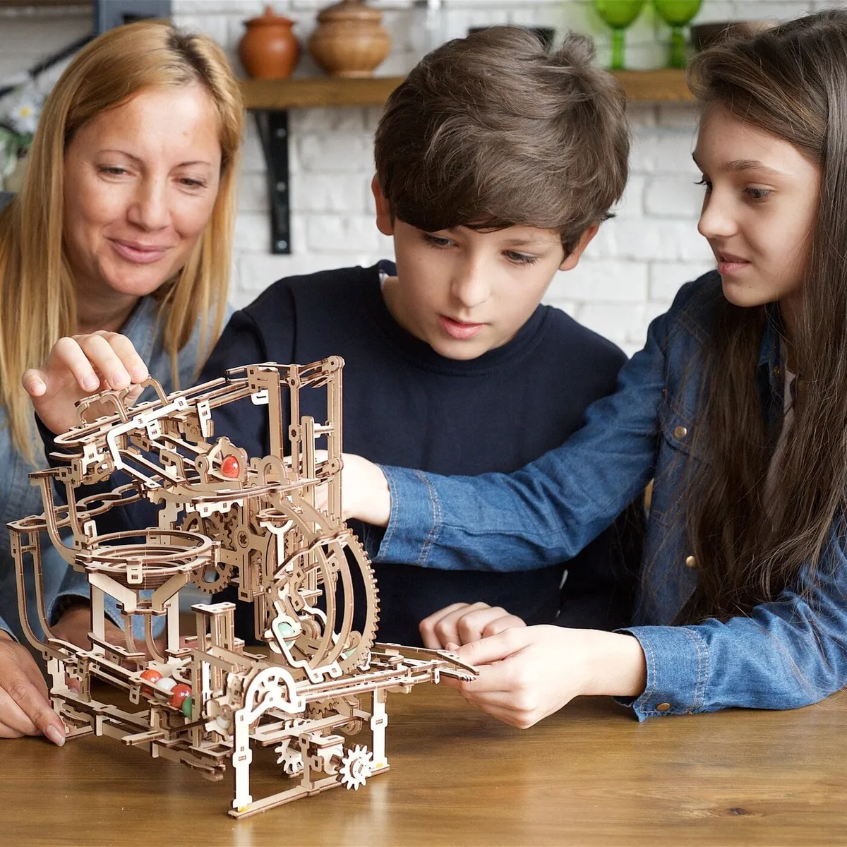 Une mère et ses deux enfants font tourner le circuit à billes en bois sur la table de la cuisine