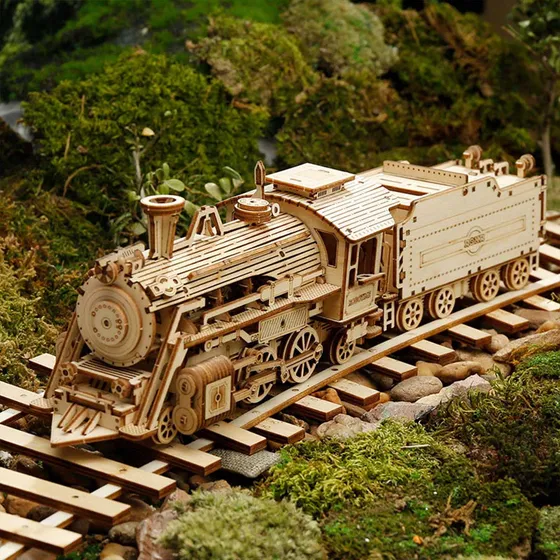 Locomotive en bois sur ses rails traversant un décor de mousse verte et de galets