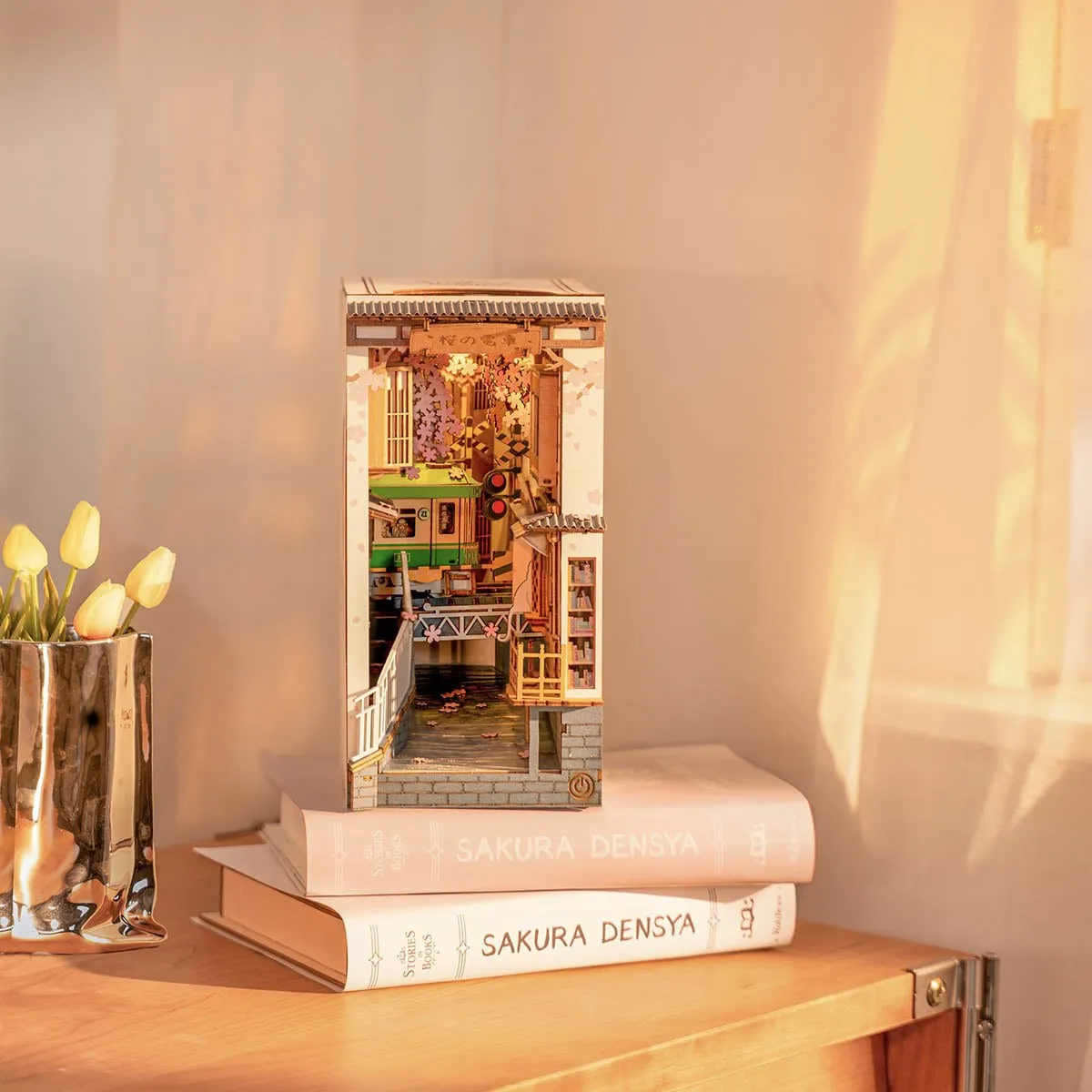 Le book nook éclairé posé sur des livres, près d’un vase de tulipes