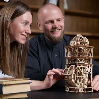 Un couple regarde fonctionner la pendulette en bois posée sur une table, à côté de livres