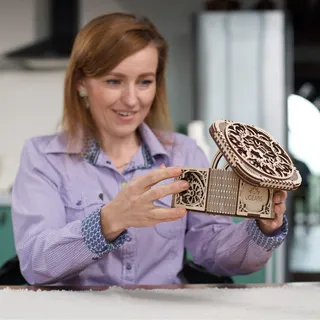 Une femme souriante ouvre le coffre au trésor en bois, assise dans une cuisine