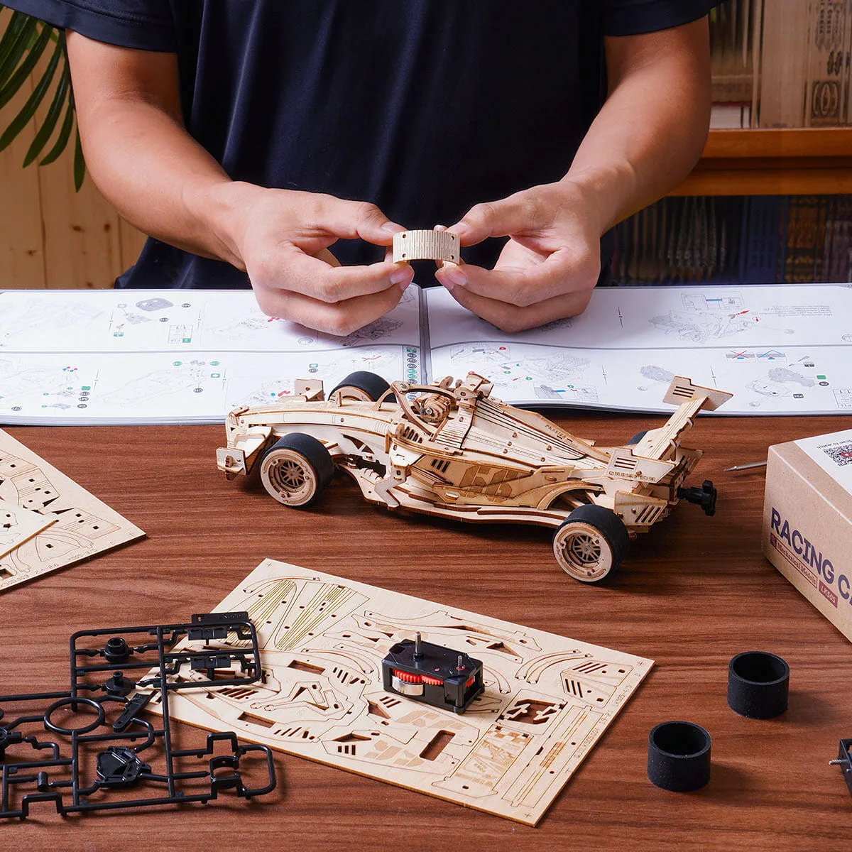 Mains assemblant une pièce de la voiture, notice et pneus sur la table