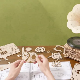 Mains assemblant des pièces d'engrenage au-dessus de la notice ouverte, gramophone monté à côté