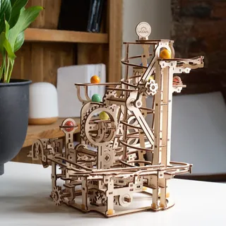 Le modèle sur une table blanche devant une étagère en bois, plante verte à gauche