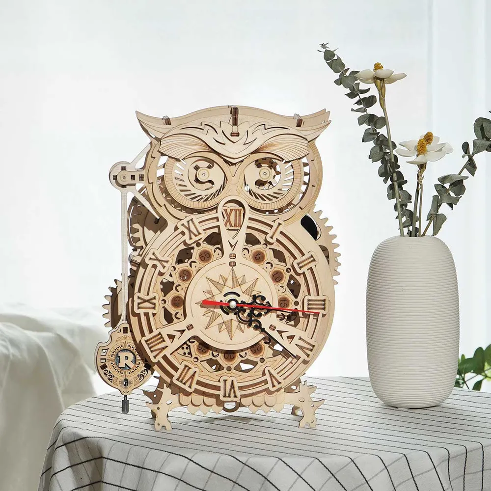 Horloge hibou posée sur une nappe rayée près d'un vase blanc garni d'eucalyptus séché