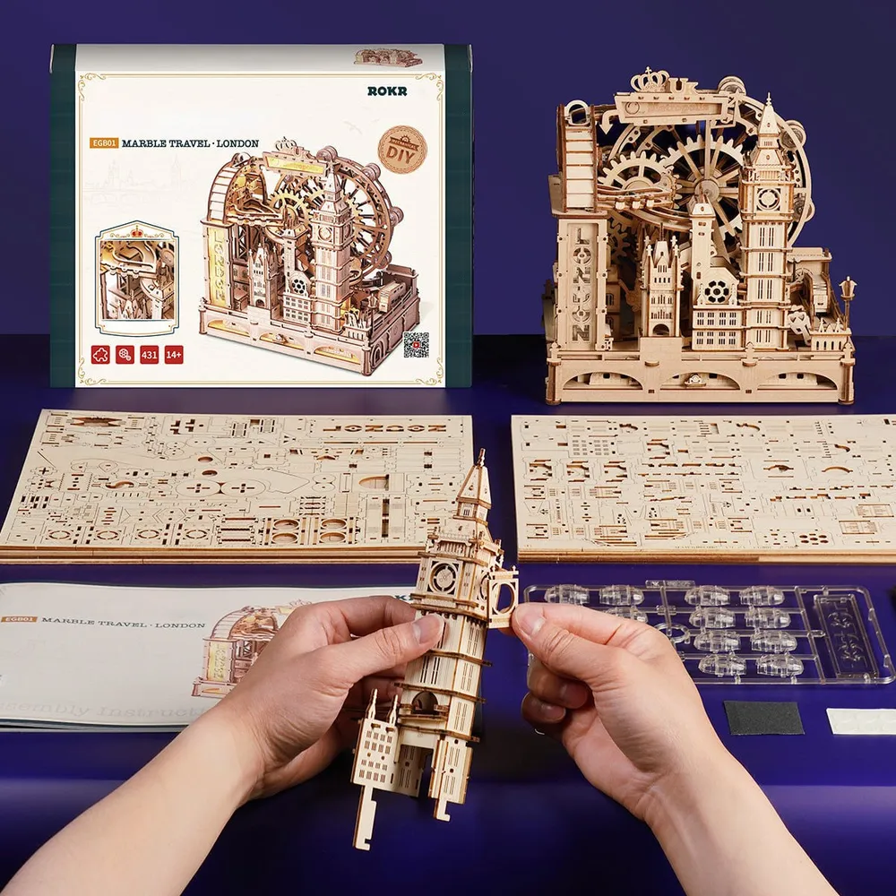 Deux mains assemblent la tour de Big Ben au-dessus des planches du kit, devant la boîte et la maquette terminée