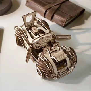Le roadster en bois portière et capot ouverts, posé sur une table à côté d’une trousse en cuir