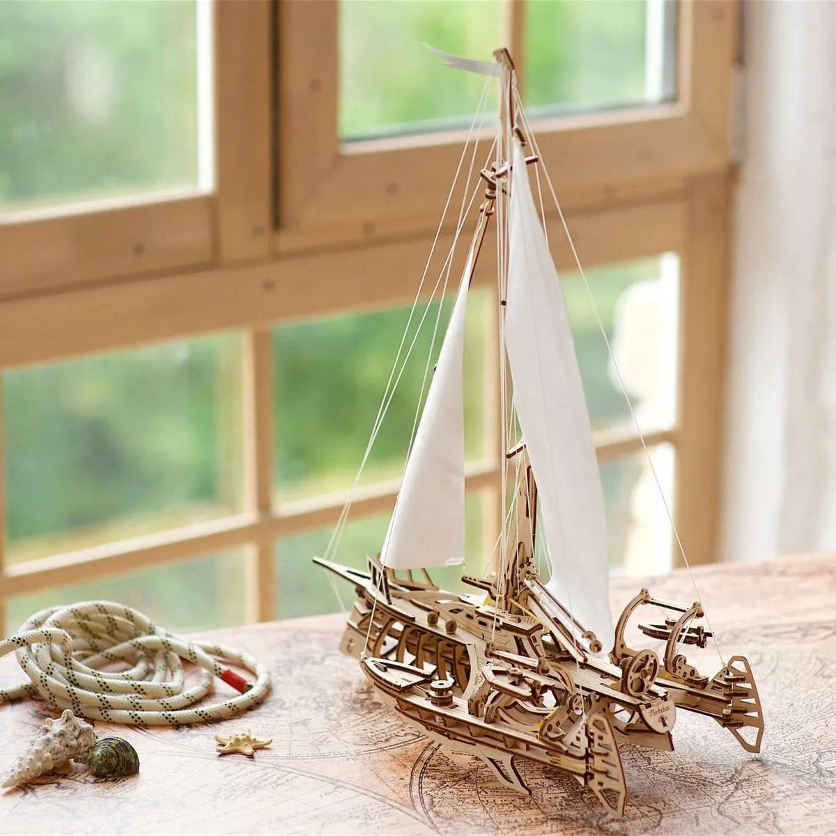 Le trimaran en bois sur une table près d’une fenêtre, à côté d’un cordage et de coquillages