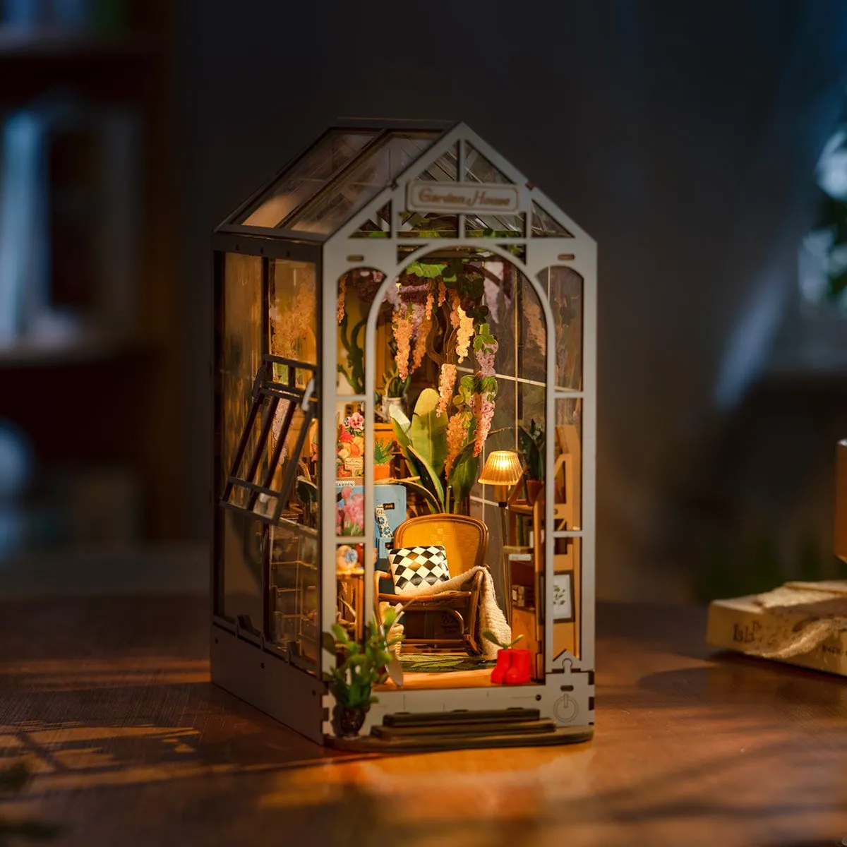 Le book nook allumé le soir sur une table, lumière chaude derrière les vitres