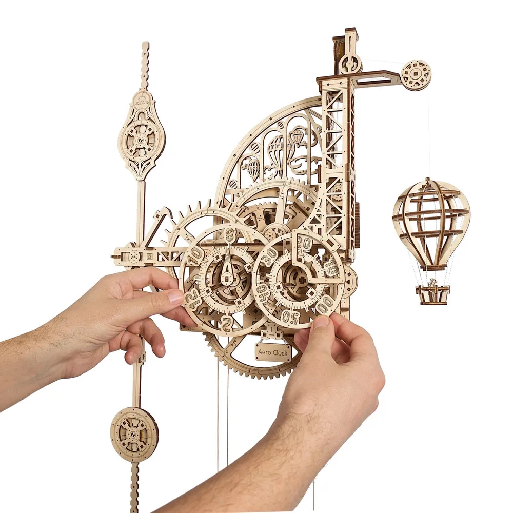 Deux mains règlent les cadrans en bois d'une horloge mécanique à engrenages apparents