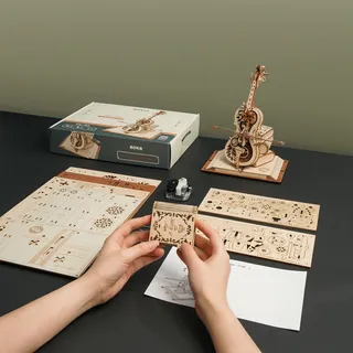 Mains assemblant une pièce devant les planches prédécoupées, la boîte et la notice
