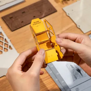 Deux mains assemblent une petite étagère jaune « Welcome to garden »