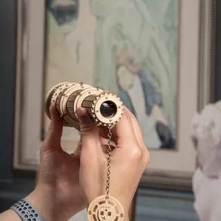 Une main tient le tube en bois devant un tableau encadré, dans un intérieur lumineux