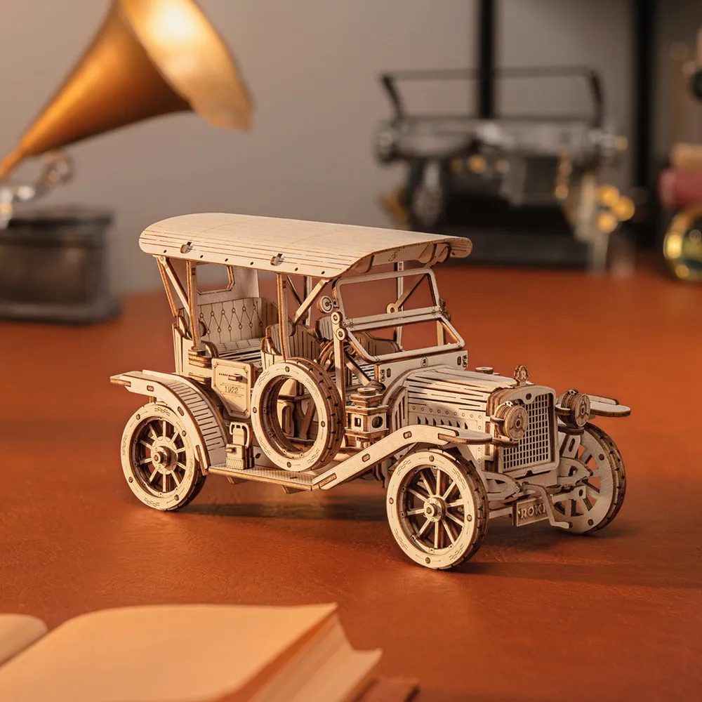 Voiture ancienne en bois devant un gramophone doré, un livre ouvert au premier plan