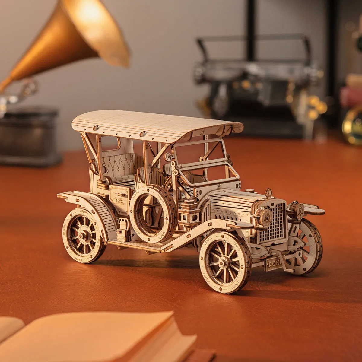 Voiture ancienne en bois devant un gramophone doré, un livre ouvert au premier plan