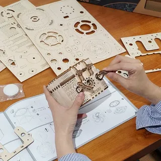 Mains en train d'assembler la boîte au-dessus des planches de bois et de la notice ouverte