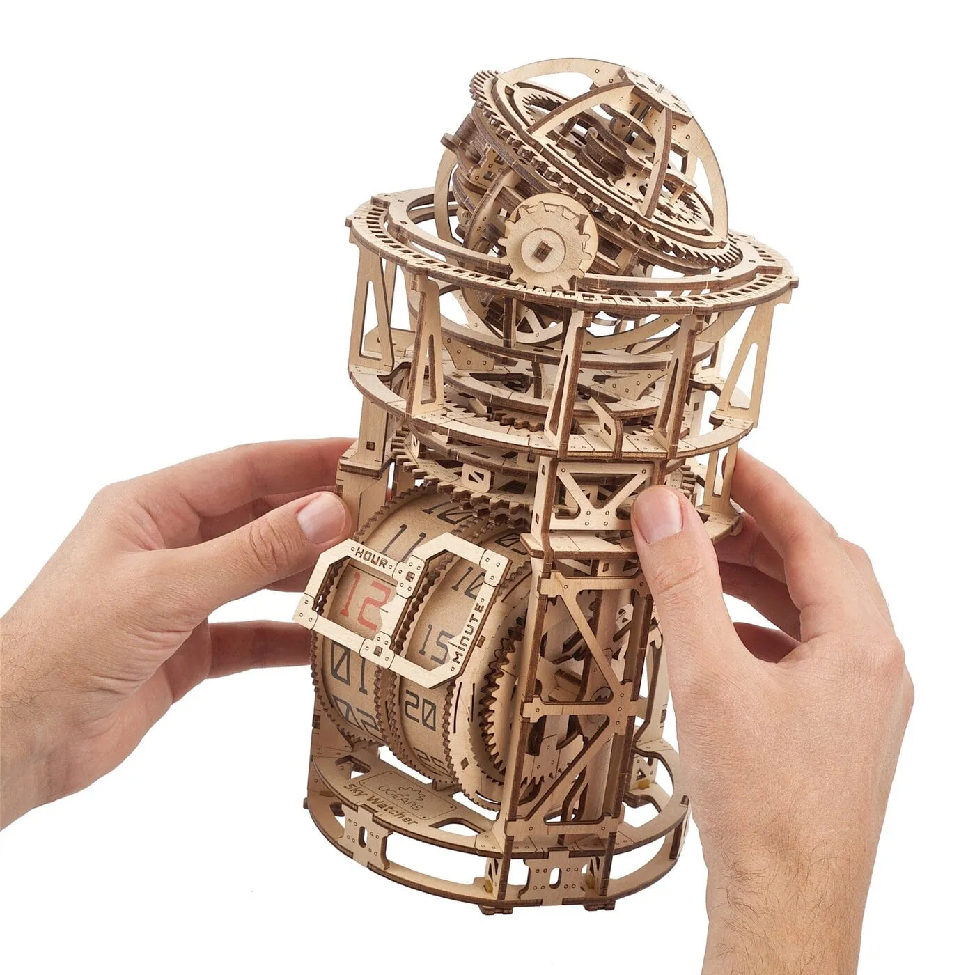 Deux mains tiennent la pendulette en bois, rouleaux de l’heure et tourbillon au sommet bien visibles